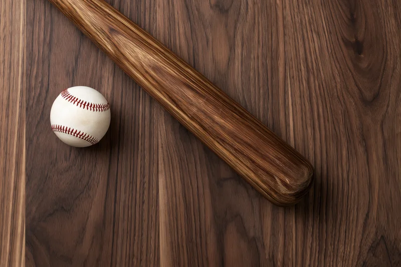 Wooden baseball bat and white leather ball resting on dark wood surface