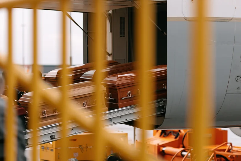 Wooden coffins being loaded onto a commercial aircraft via a cargo door in an industrial facility