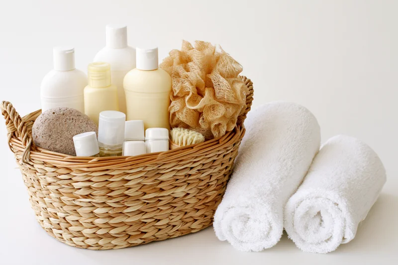 Woven basket filled with toiletries and rolled towels on white surface
