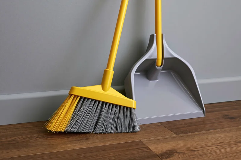 Yellow-handled broom and matching grey dustpan leaning against a wall on a wooden floor