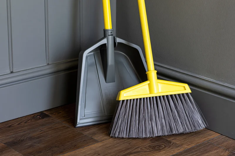 Yellow-handled broom and matching grey dustpan leaning against a grey wall in a home interior