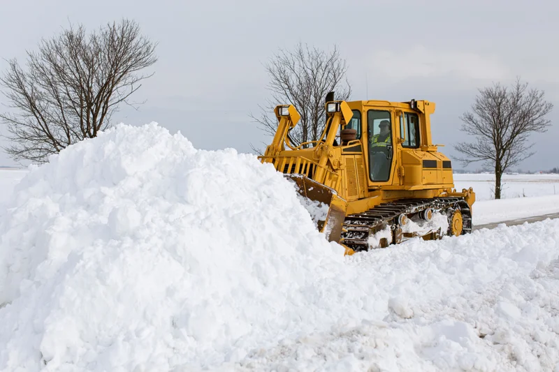 Yellow bulldozer pushing snow on a rural road in winter