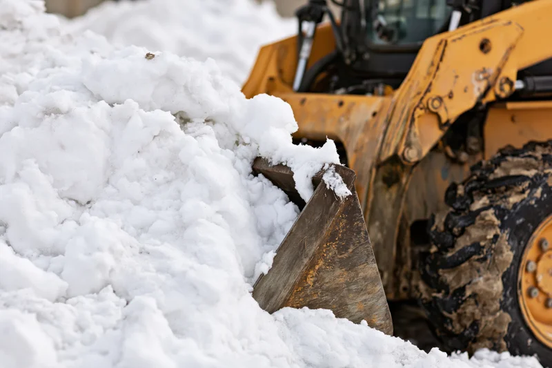 Yellow skid steer front-loader pushing snow with bucket in winter outdoor setting