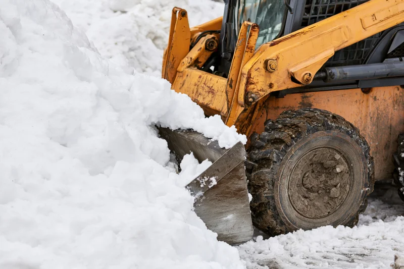 Yellow skid steer pushing snow with bucket in winter outdoor setting