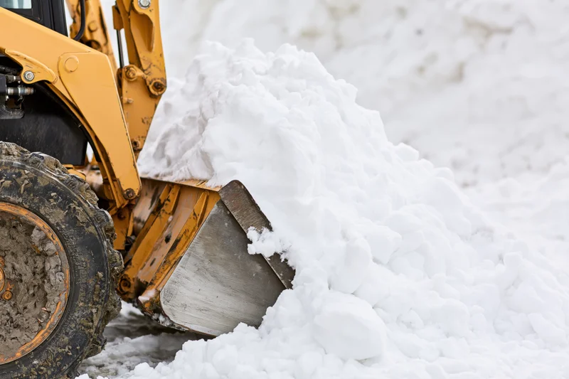 Yellow skid steer front loader pushing snow with bucket in winter outdoor setting