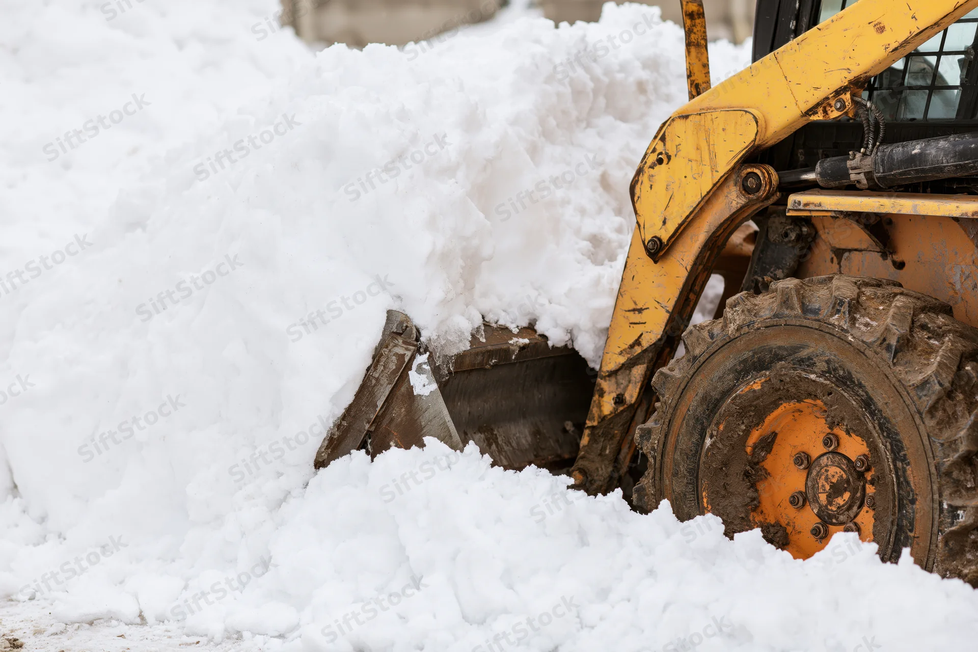 Yellow skid steer pushing snow with bucket in winter outdoor setting