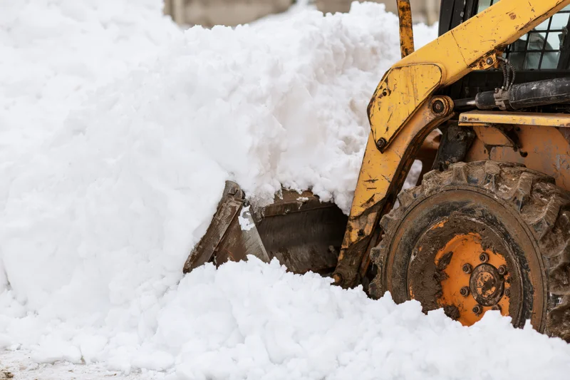 Yellow skid steer pushing snow with bucket in winter outdoor setting
