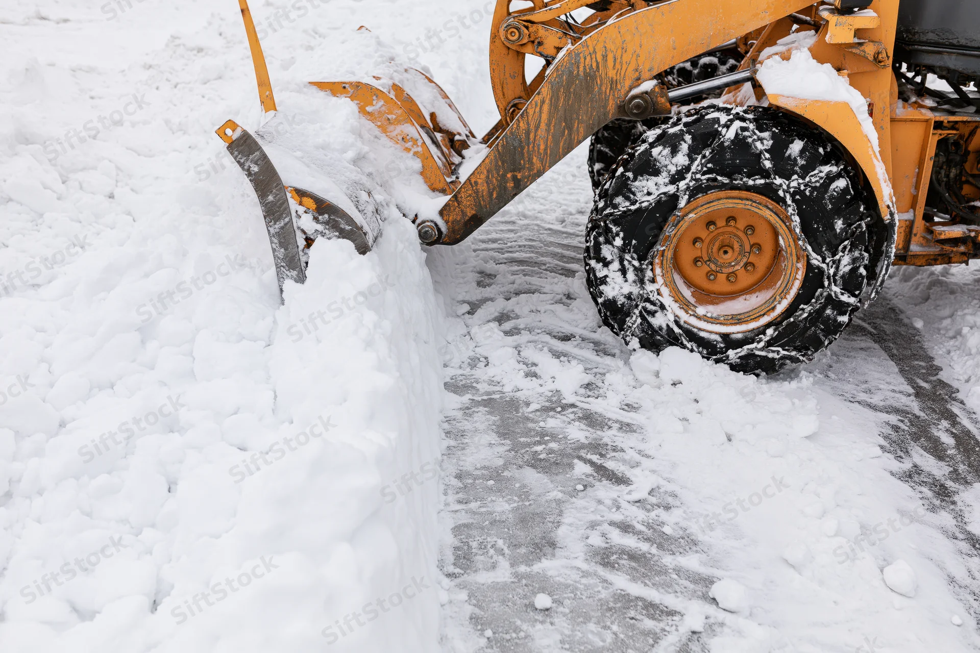 Yellow wheel loader pushing packed snow on paved surface