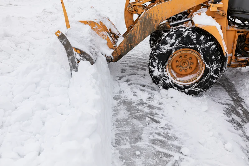 Yellow wheel loader pushing packed snow on paved surface
