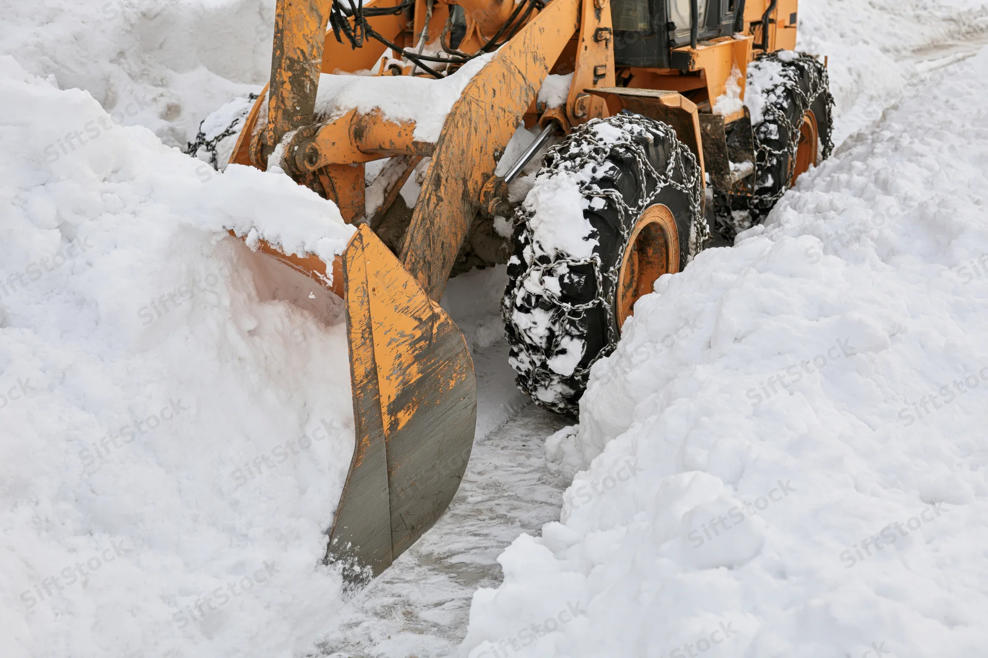 Yellow wheel loader pushing snow on a snowy road