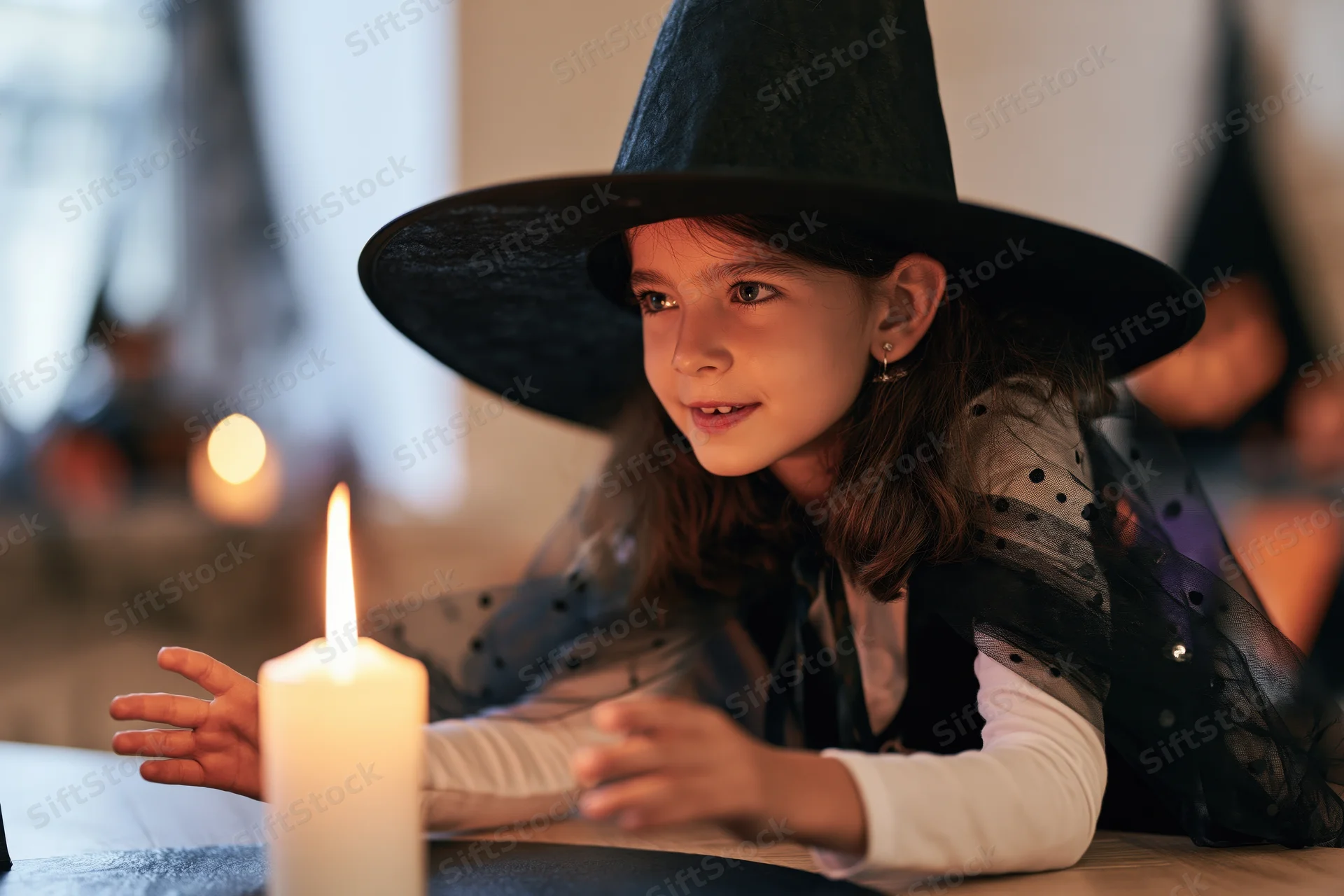 Young girl in witch costume with candle on table during halloween celebration
