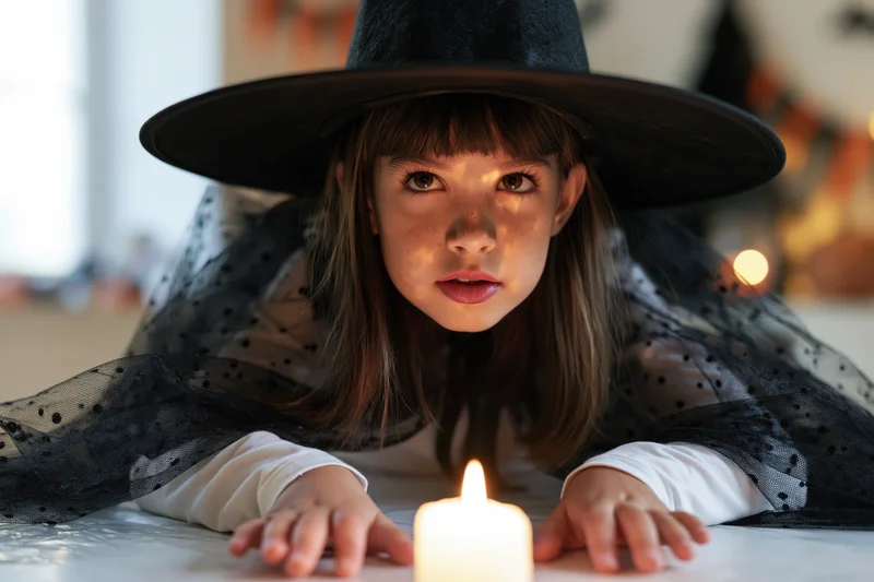 Young girl in witch costume lying on table with candle in front of her