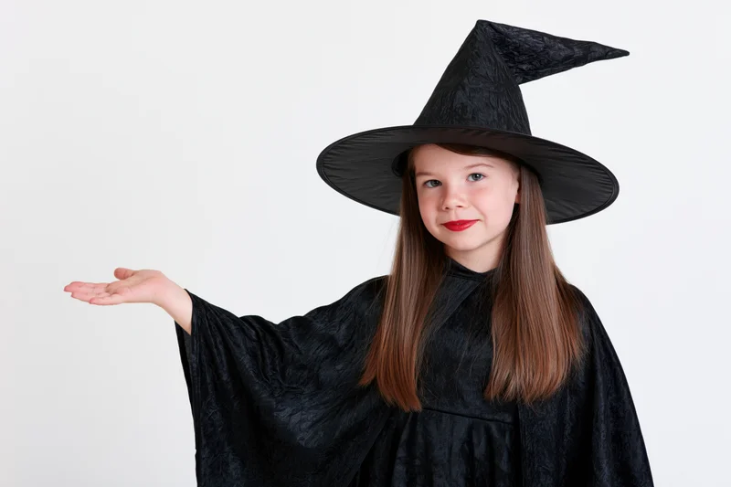 Young girl in black witch costume pointing with hand extended against white background