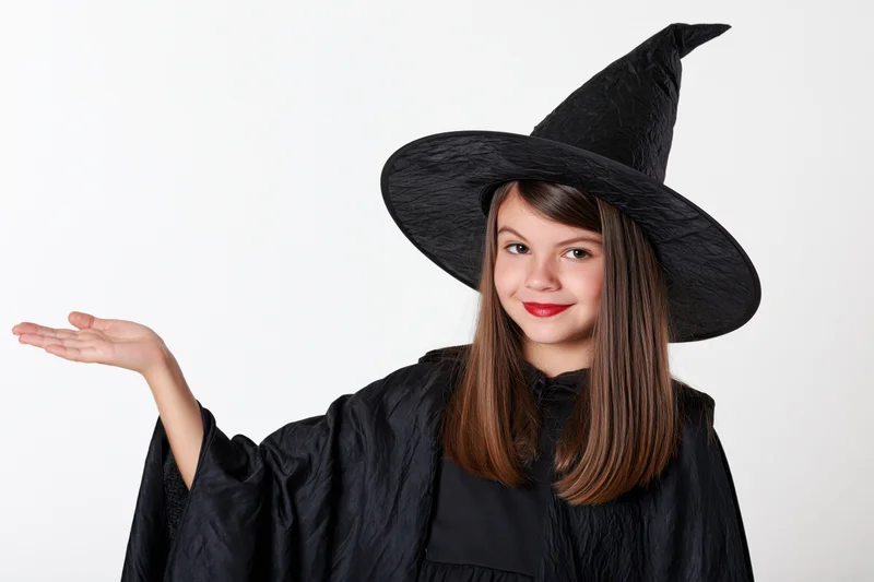 Young girl in black witch costume pointing with hand extended against white background