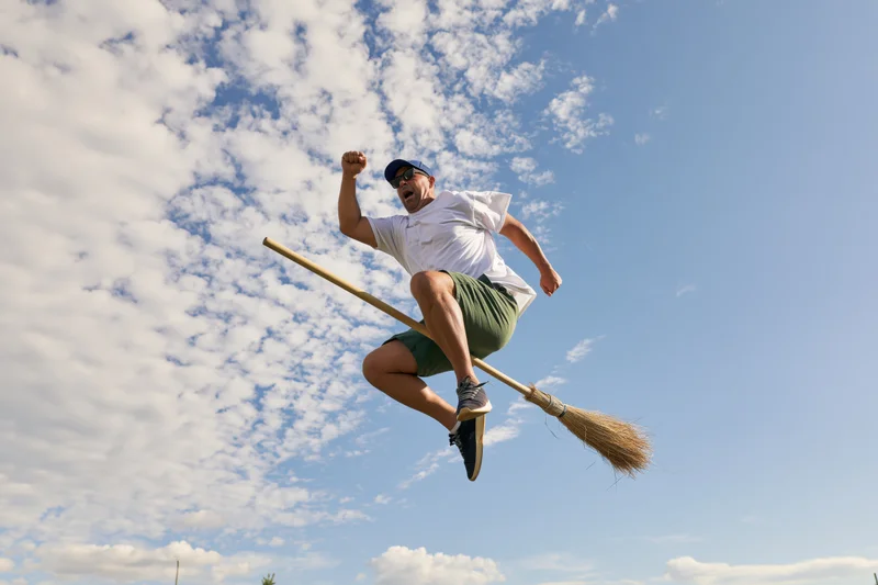 Man flying on a straw broom with fist raised against a cloudy sky