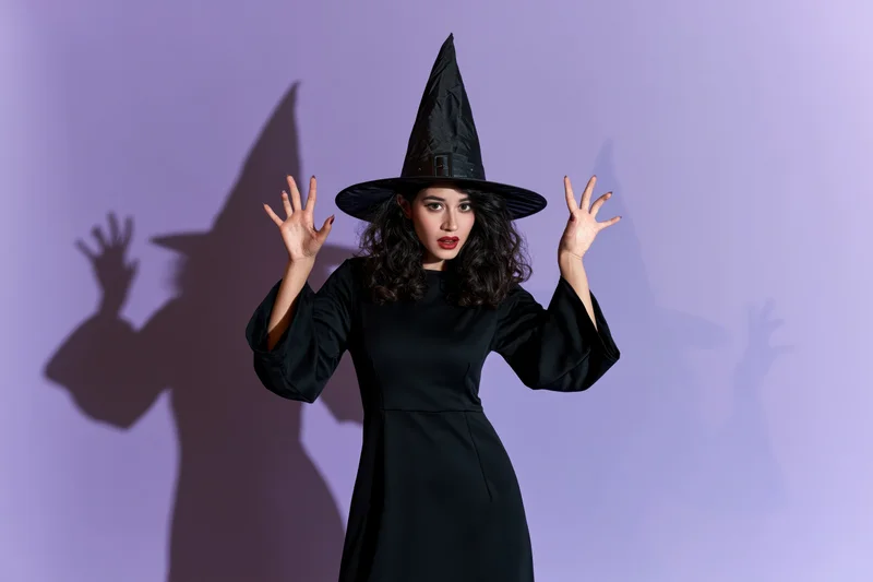Woman in black witch costume raising hands against purple background