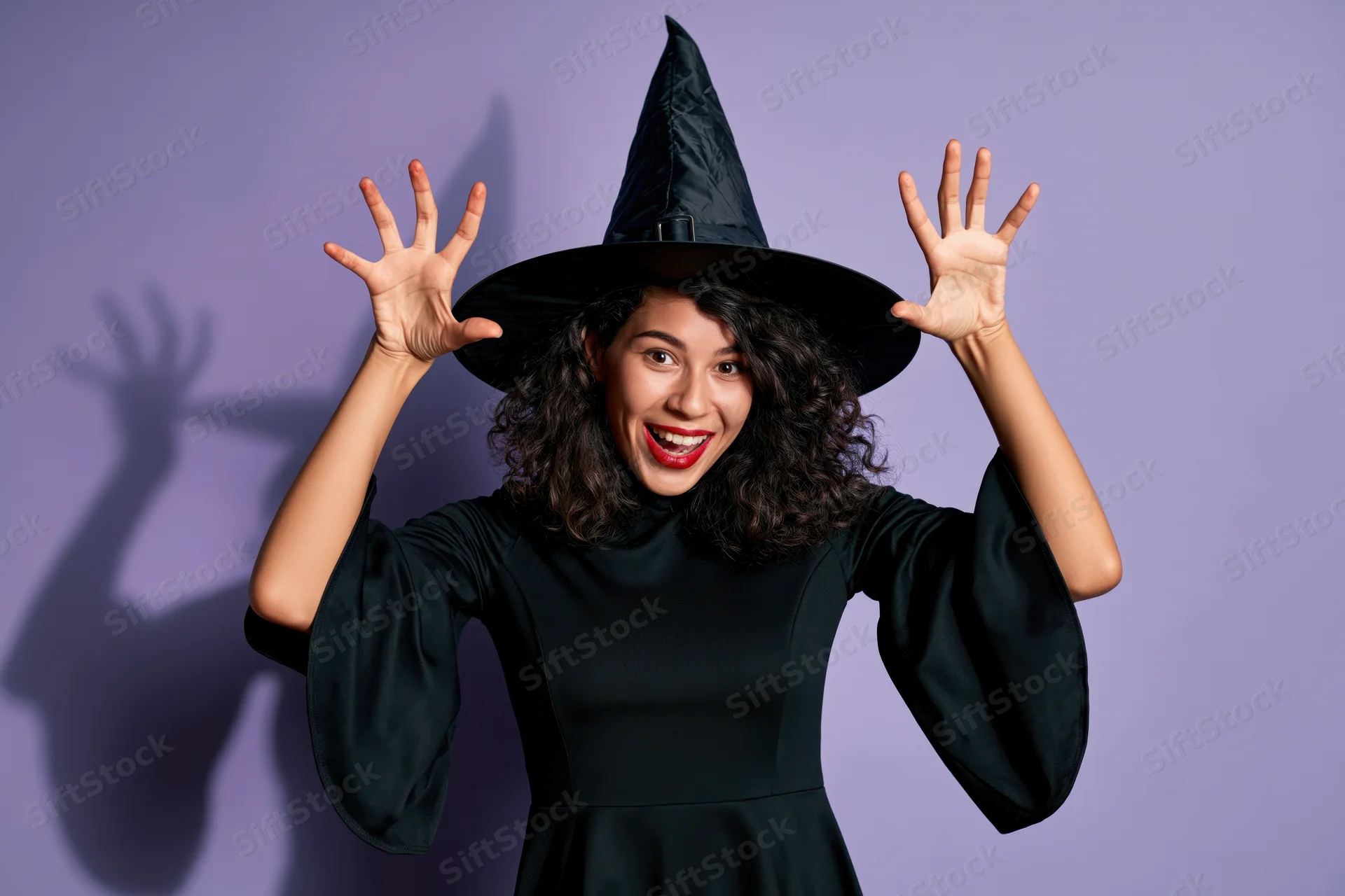 Woman in black witch costume raising hands with smile against purple background