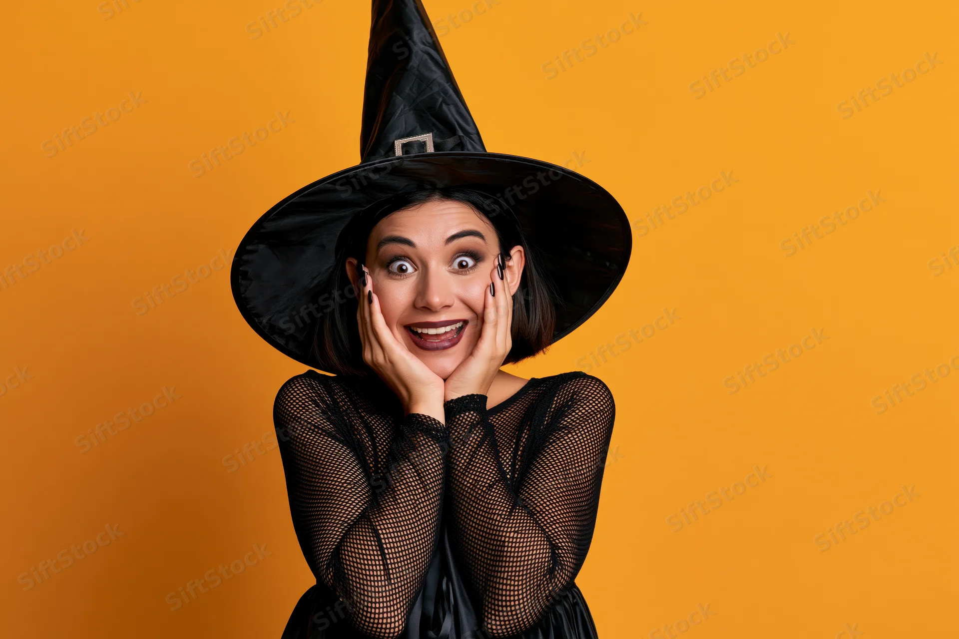 Woman in black witch costume with hands on cheeks against orange background