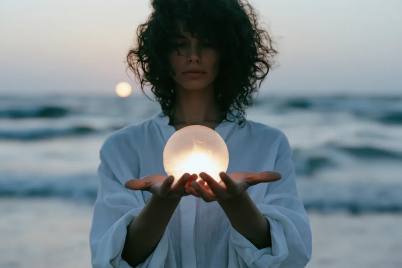 Young woman holding glowing sphere on beach at twilight