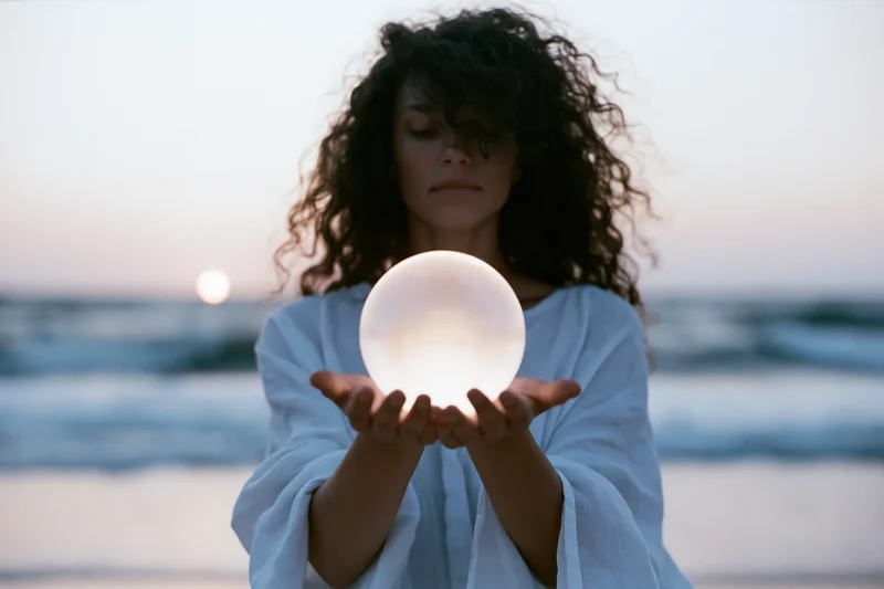 Woman holding glowing sphere on beach at sunset