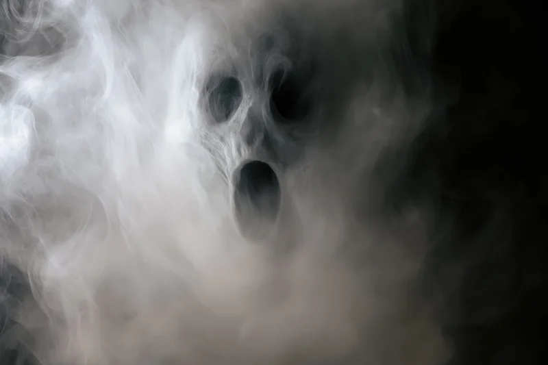 Ghostly face emerging from swirling white smoke in dark atmosphere