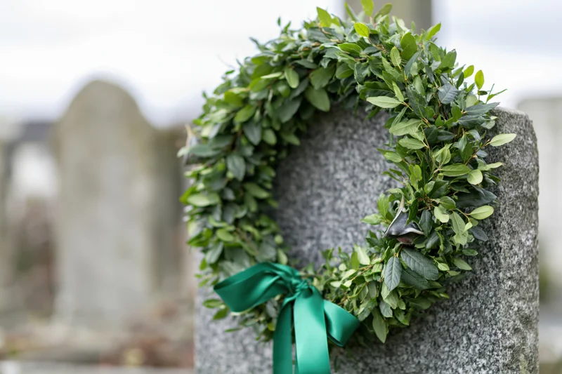 Green leafy funeral wreath with satin ribbon resting on a gray stone grave in a cemetery