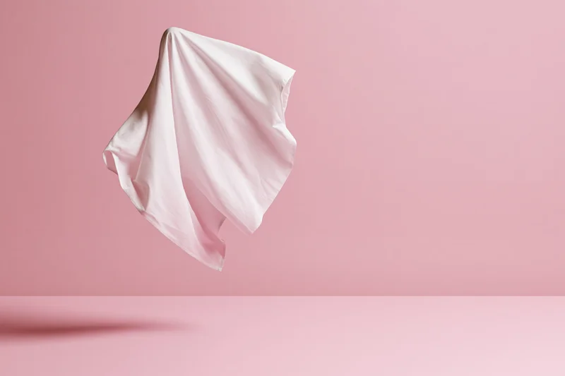 White fabric sheet floating in midair against pink background