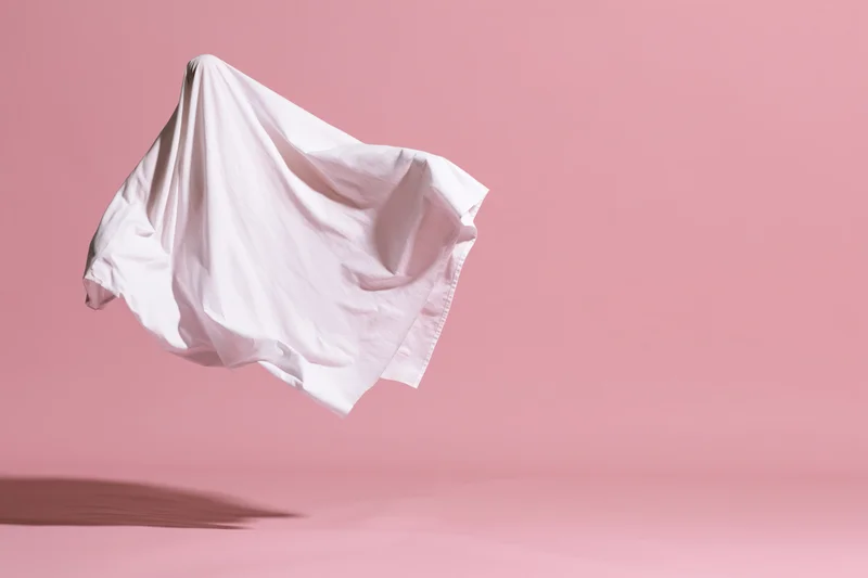 White fabric sheet floating in midair against pink background