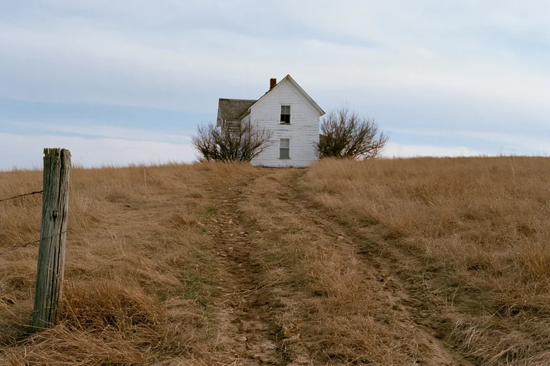 Abandoned white clapboard farmhouse on a grassy hill with a dirt path leading up to it