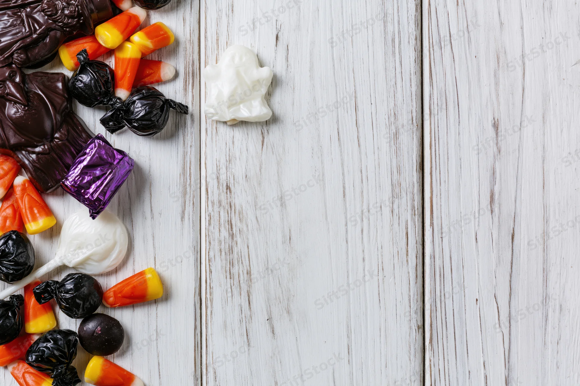 Assorted halloween candy scattered on white wooden surface with copyspace