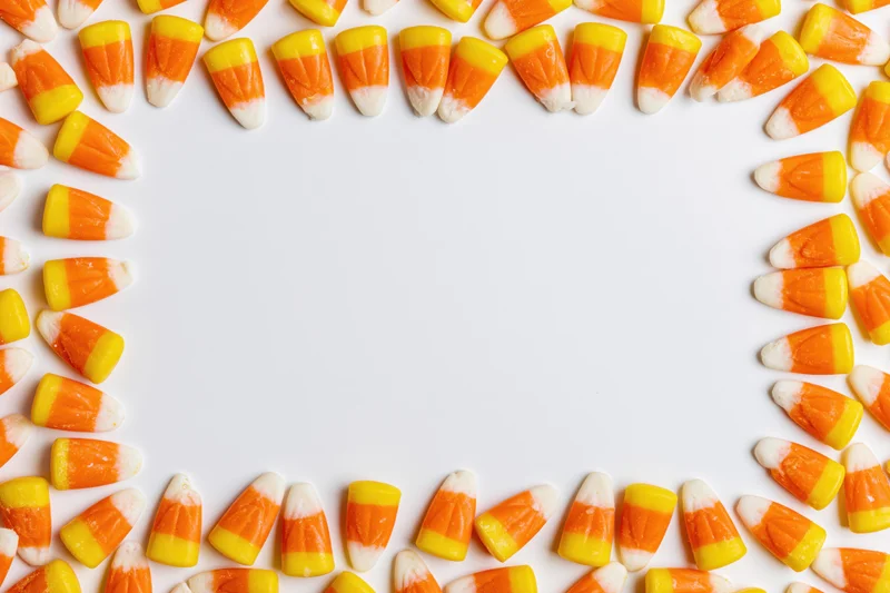 Candy corn pieces arranged in a loose rectangular border frame on white background with copyspace