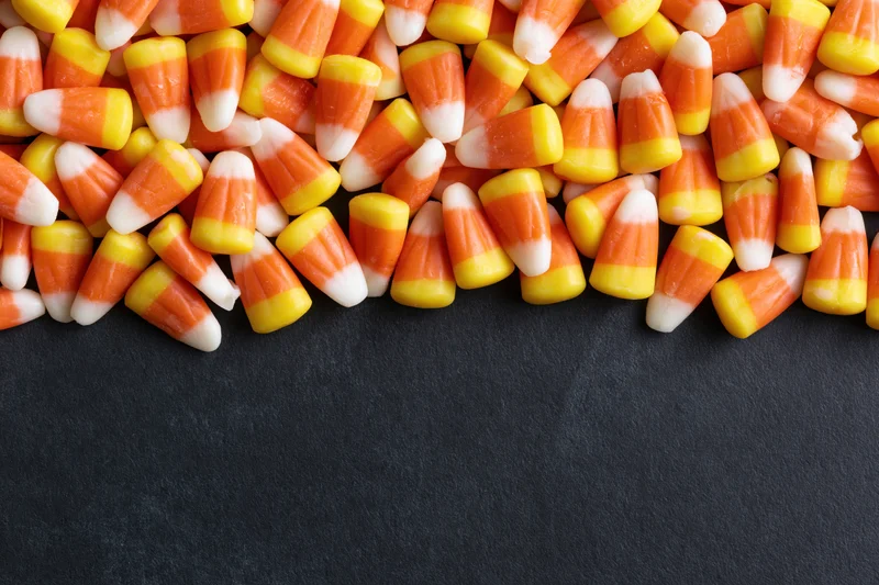 Candy corn pieces scattered densely across the top edge of a dark surface with copyspace below