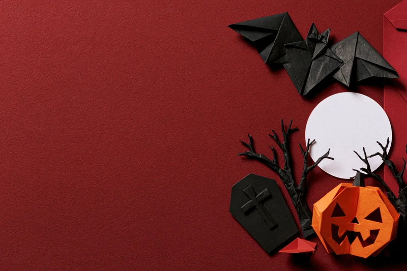 Handmade paper origami halloween decorations arranged on red surface with copyspace