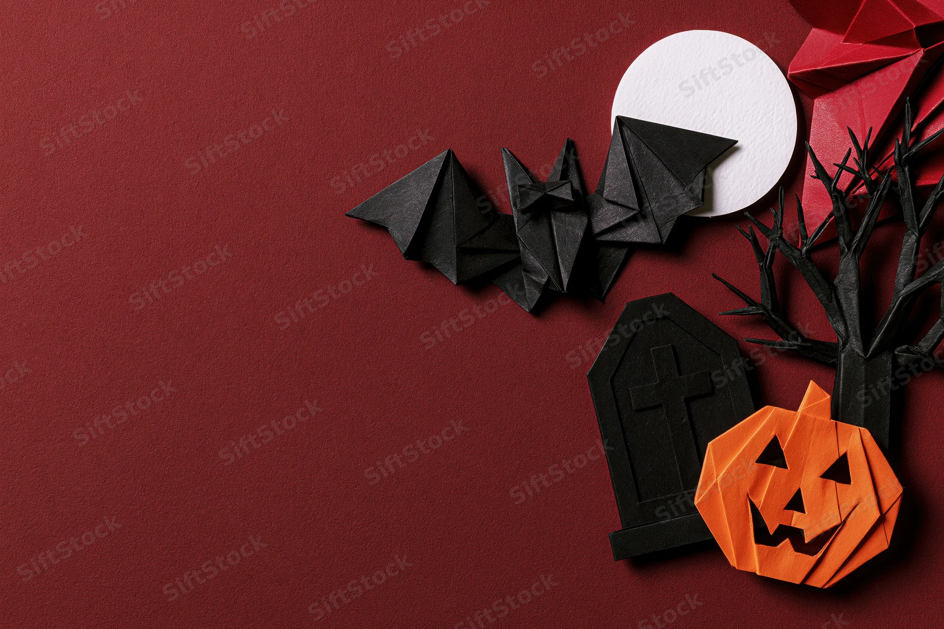 Handmade paper origami halloween decorations arranged in flat lay on red background with copyspace