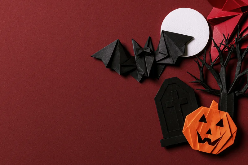Handmade paper origami halloween decorations arranged in flat lay on red background with copyspace