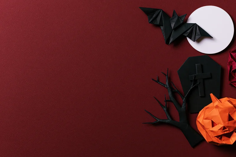 Handmade paper origami halloween decorations arranged on red surface with copyspace