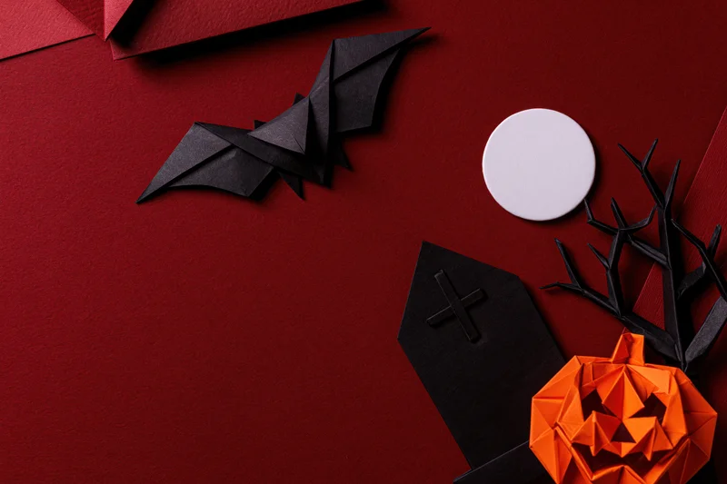 Handmade paper origami halloween decorations arranged in flat lay on red surface with copyspace
