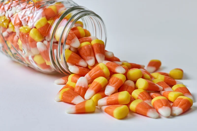 Candy corn pieces spilling from a tipped glass mason jar onto a white surface