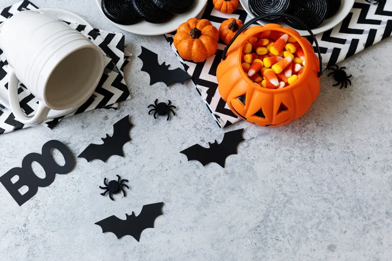 Halloween flat lay with candy corn in pumpkin bucket, bats, spiders, and cookies on concrete surface