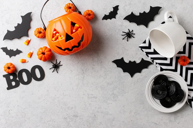 Halloween flat lay with pumpkin bucket, candy, bats, and cookies on concrete surface