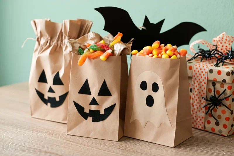 Halloween trick-or-treat kraft paper bags with jack-o-lantern and ghost faces filled with candy on a wooden table