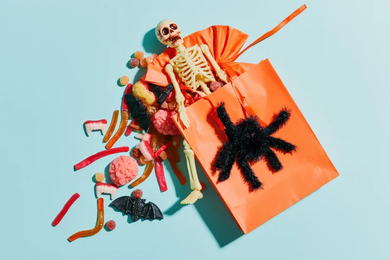 Orange paper bag filled with halloween candy and toys spilling onto a blue surface