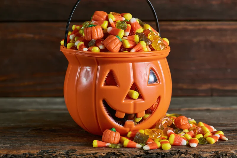Orange plastic jack-o-lantern bucket overflowing with candy on a wooden table