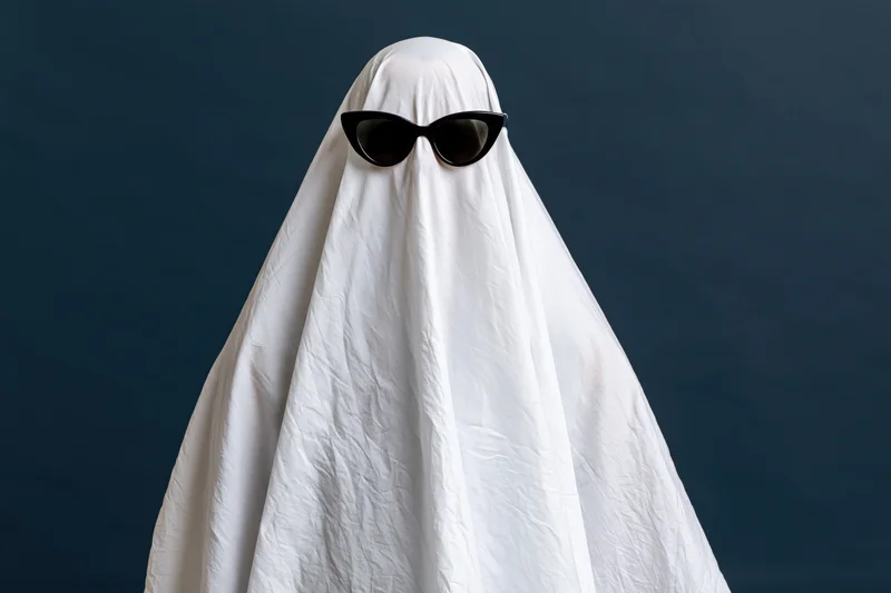 Ghost in white sheet costume wearing black sunglasses against dark background