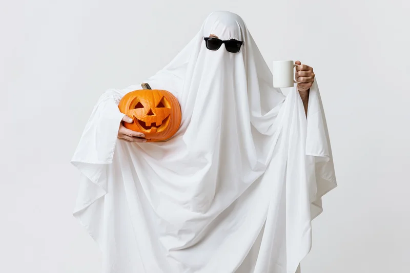 Person dressed as ghost holding pumpkin and mug in studio