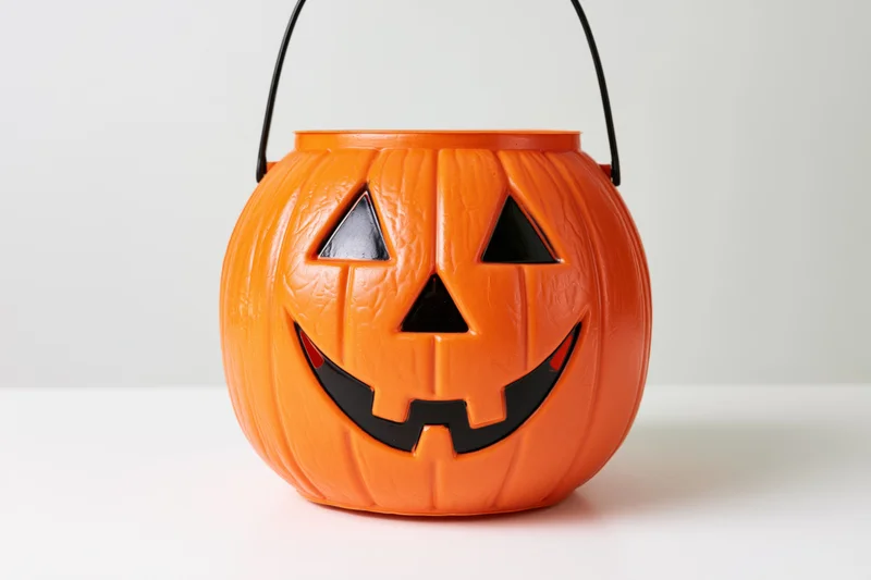Orange plastic jack-o-lantern candy bucket with carved face and black handle on white background