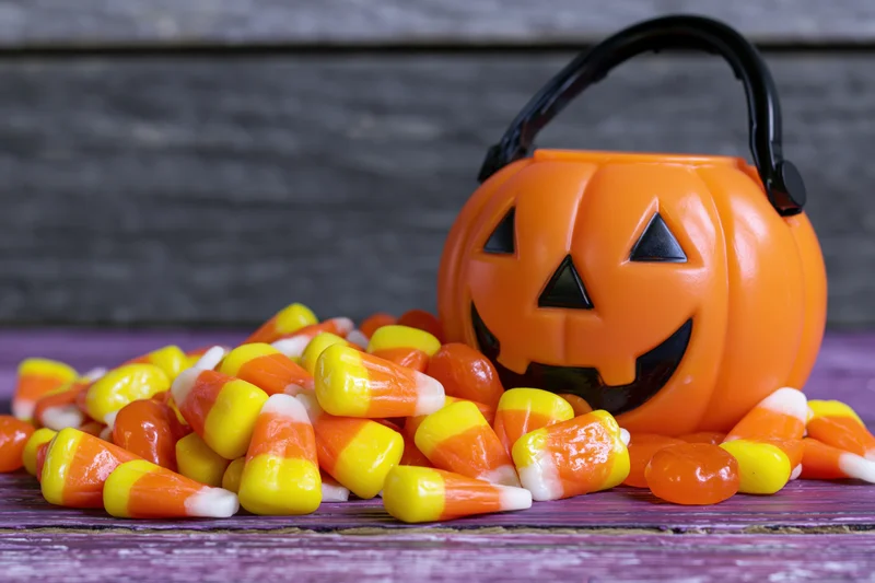 Orange plastic jack-o-lantern bucket spilling candy corn on purple wooden surface