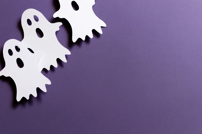 Three white paper-cut ghost decorations arranged diagonally on purple background with copyspace