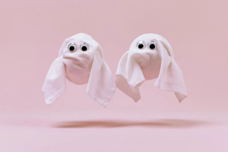 Two handmade ghost figures floating against a pink background