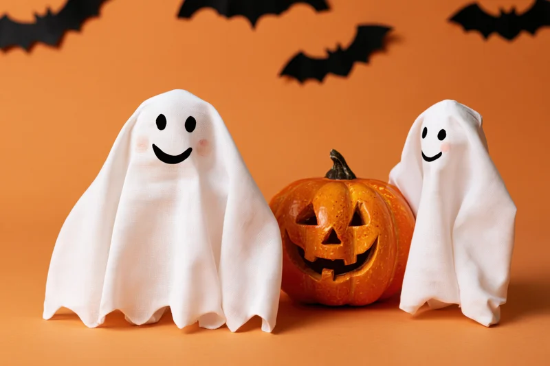 Two smiling fabric ghost decorations flanking a carved jack-o-lantern on orange background